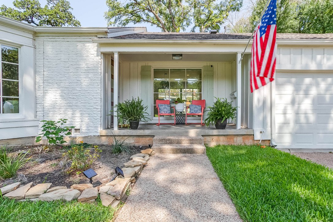 White-facade home exterior with a driveway and an American flag by the porch